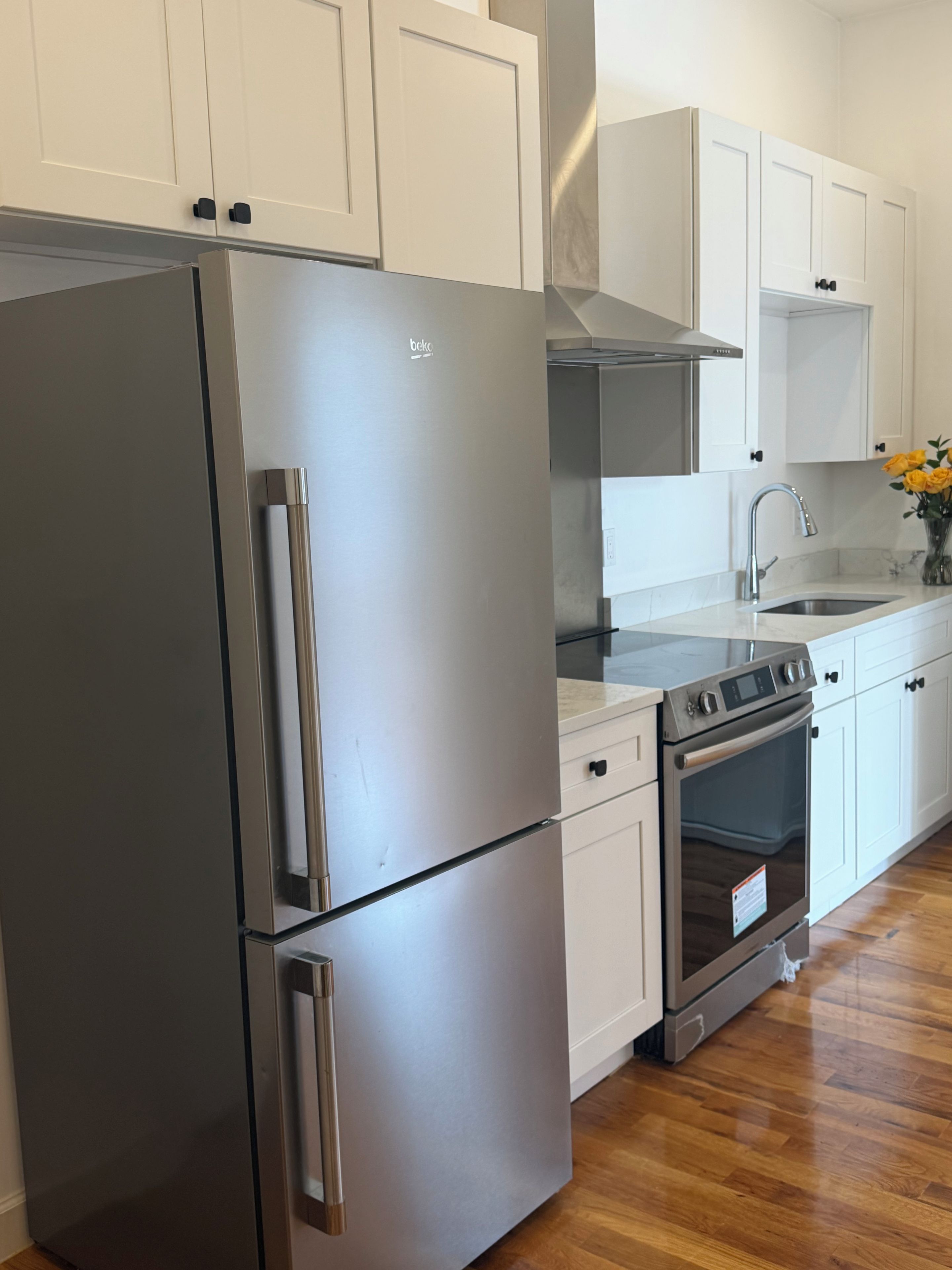 A modern kitchen with stainless steel appliances, white cabinetry, and a wooden floor.