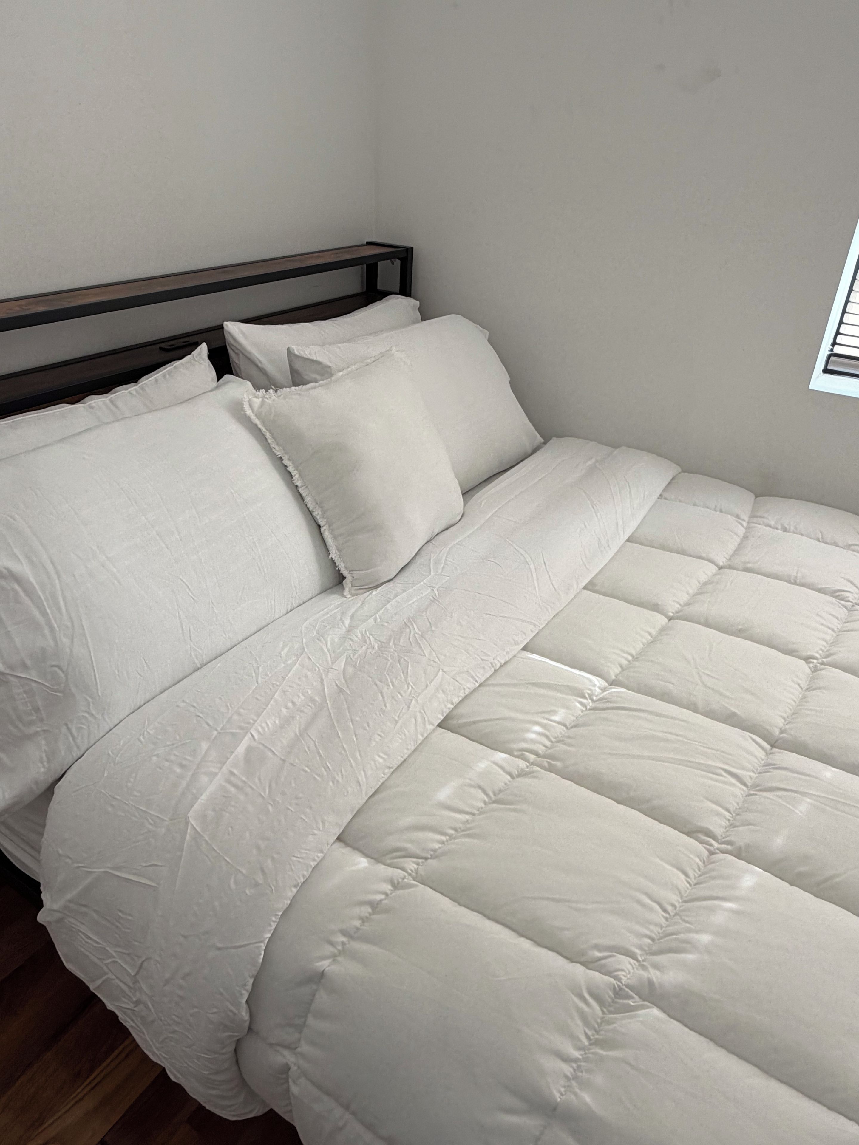 Una cama con cabecera de madera, ropa de cama blanca y una ventana con persianas.