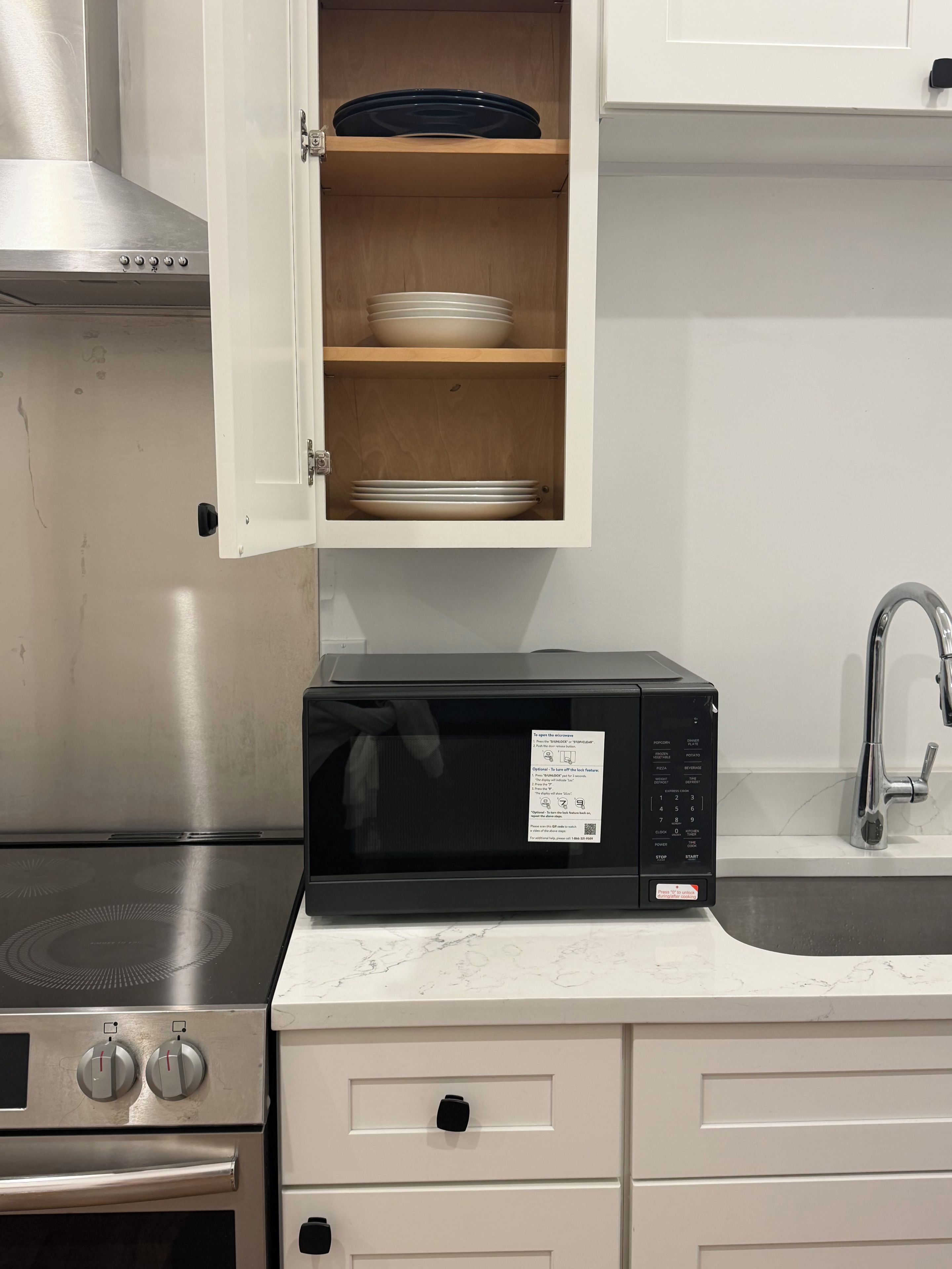 Une cuisine équipée d’un four à micro-ondes, d’une cuisinière et d’un placard contenant de la vaisselle.
