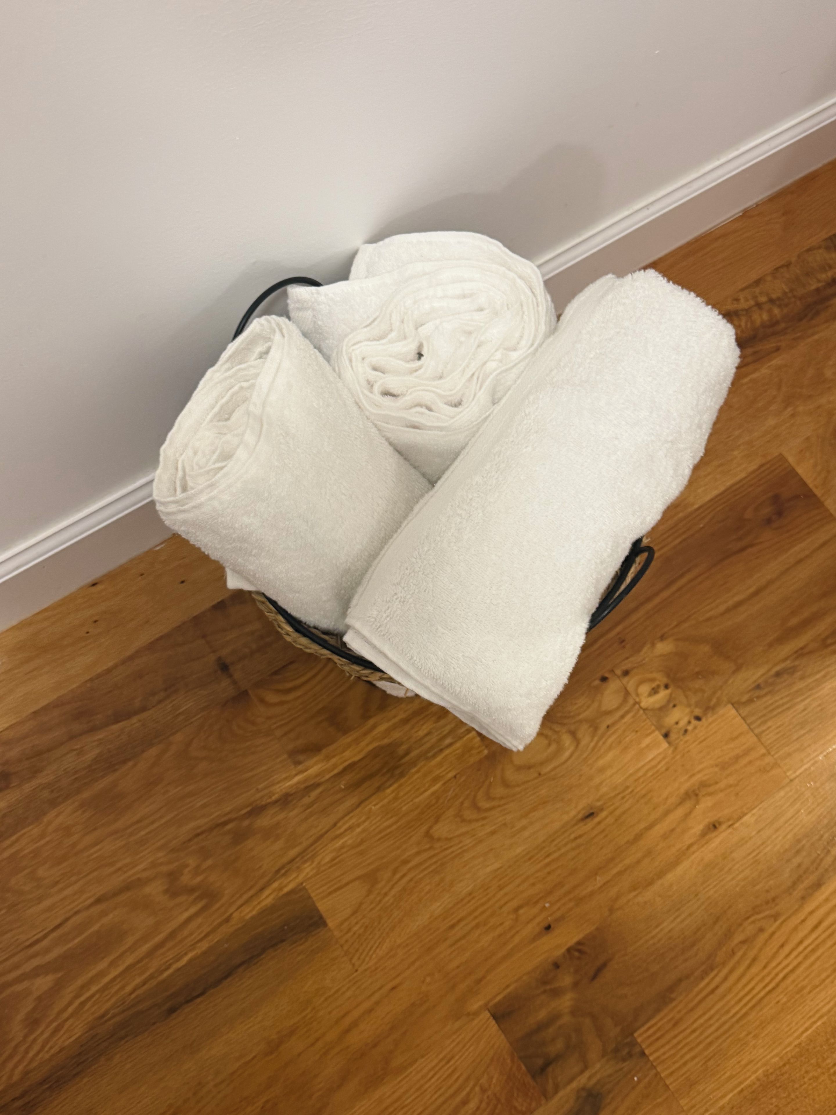 A basket with folded white towels on a wooden floor.