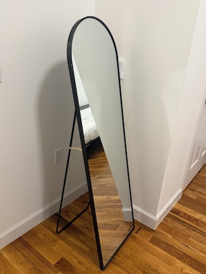 A room with a white wall, a wooden floor, and a black metal stand with a white panel.