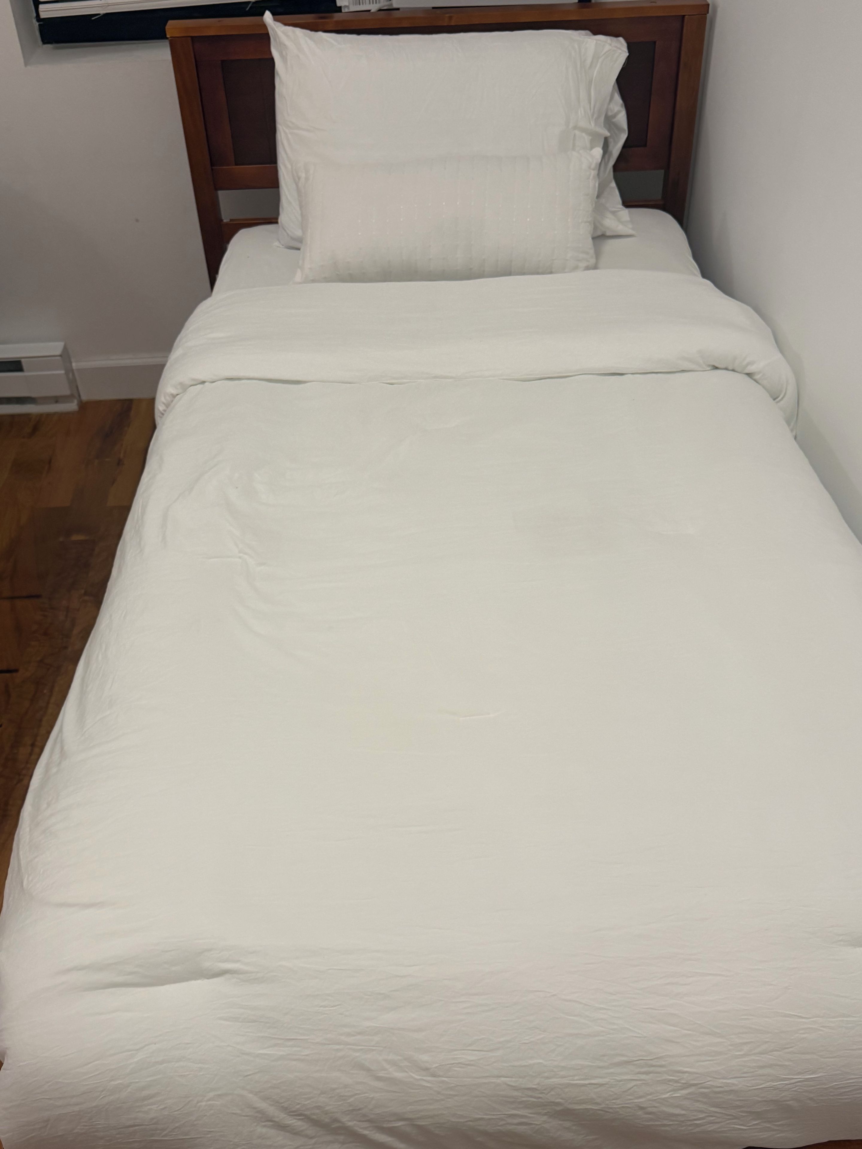 Una cama individual con cabecera de madera y ropa de cama blanca.