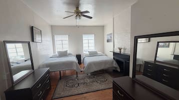 A bedroom with two beds, a ceiling fan, a rug, and a dresser.