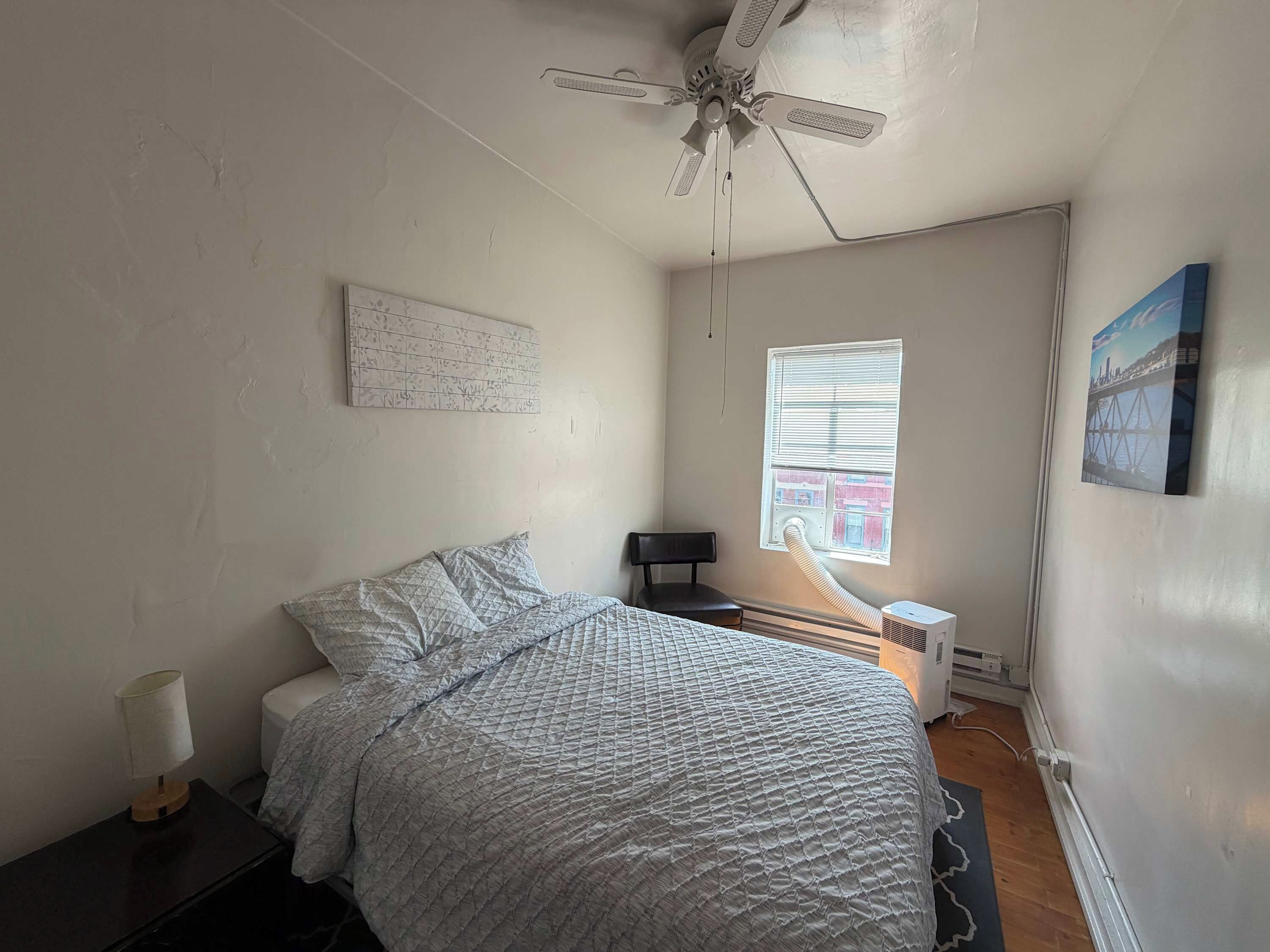 A bedroom with a bed, a ceiling fan, a window with blinds, a radiator, and a wall-mounted picture.