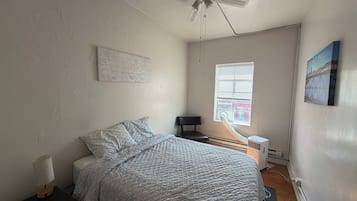 A bedroom with a bed, a ceiling fan, a window with blinds, a radiator, and a wall-mounted picture.