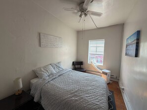 A bedroom with a bed, a ceiling fan, a window with blinds, a radiator, and a wall-mounted picture. - Budget 2BR Crash Pad  - East Carson St and Parking (Pittsburgh)