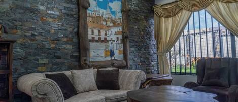 Quarto com parede de pedra, um mural, sofá, mesa de centro e janela com cortinas.