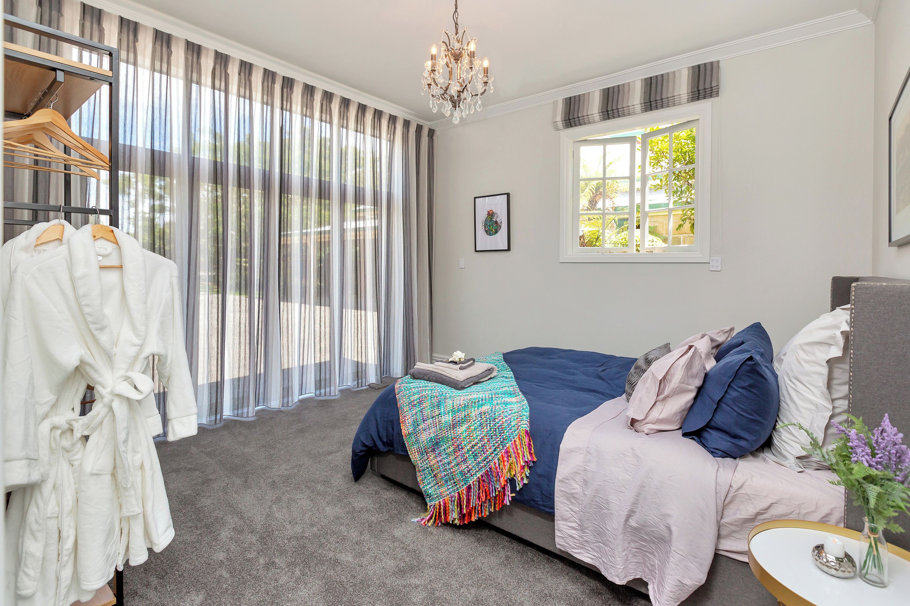 A bedroom with a bed, a bedside table, a window, and a chandelier.
