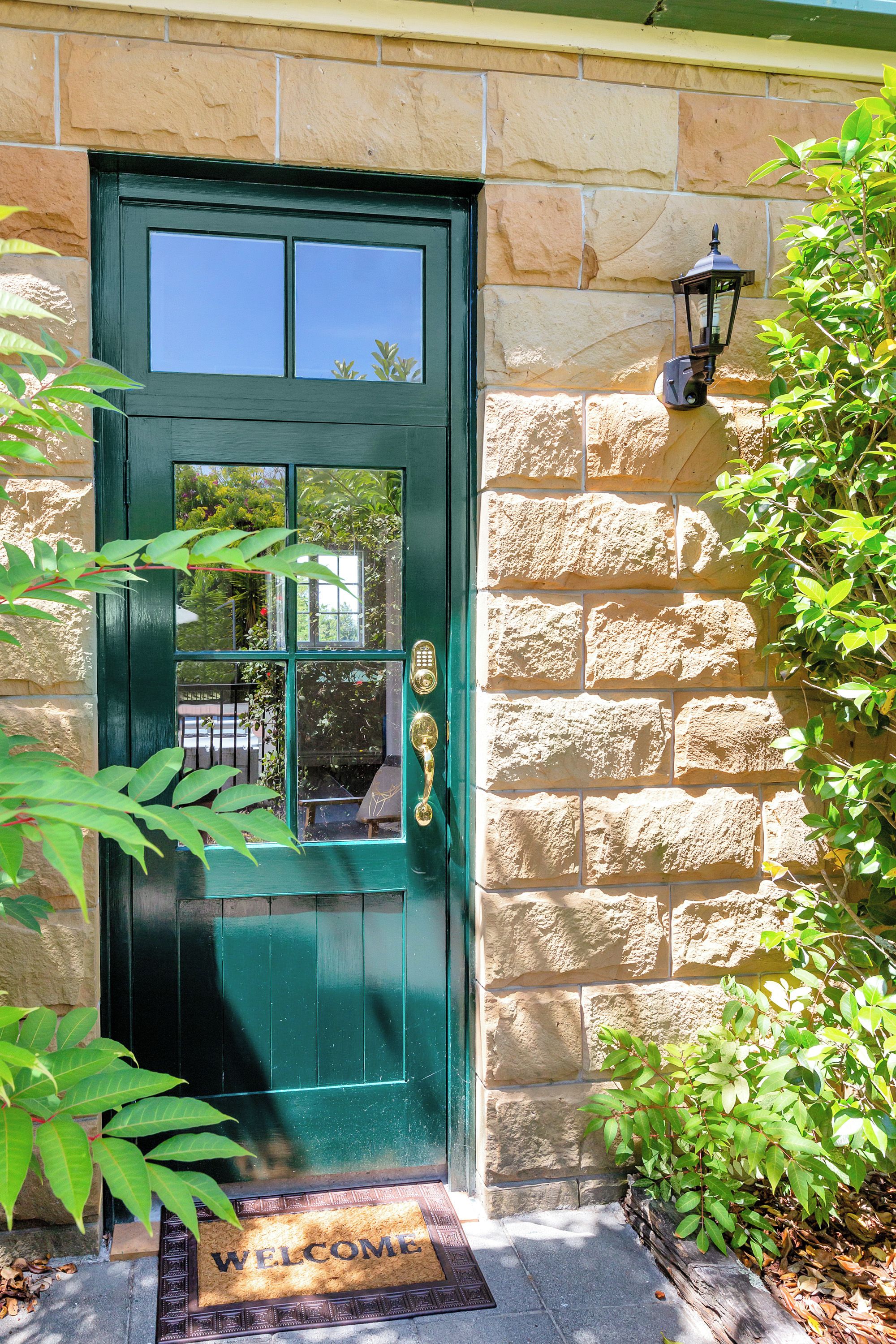 A green door with a window, a doormat with 'WELCOME' written on it, and a stone wall.