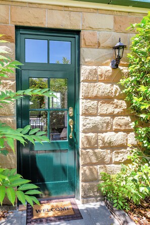 A green door with a window, a doormat with 'WELCOME' written on it, and a stone wall.