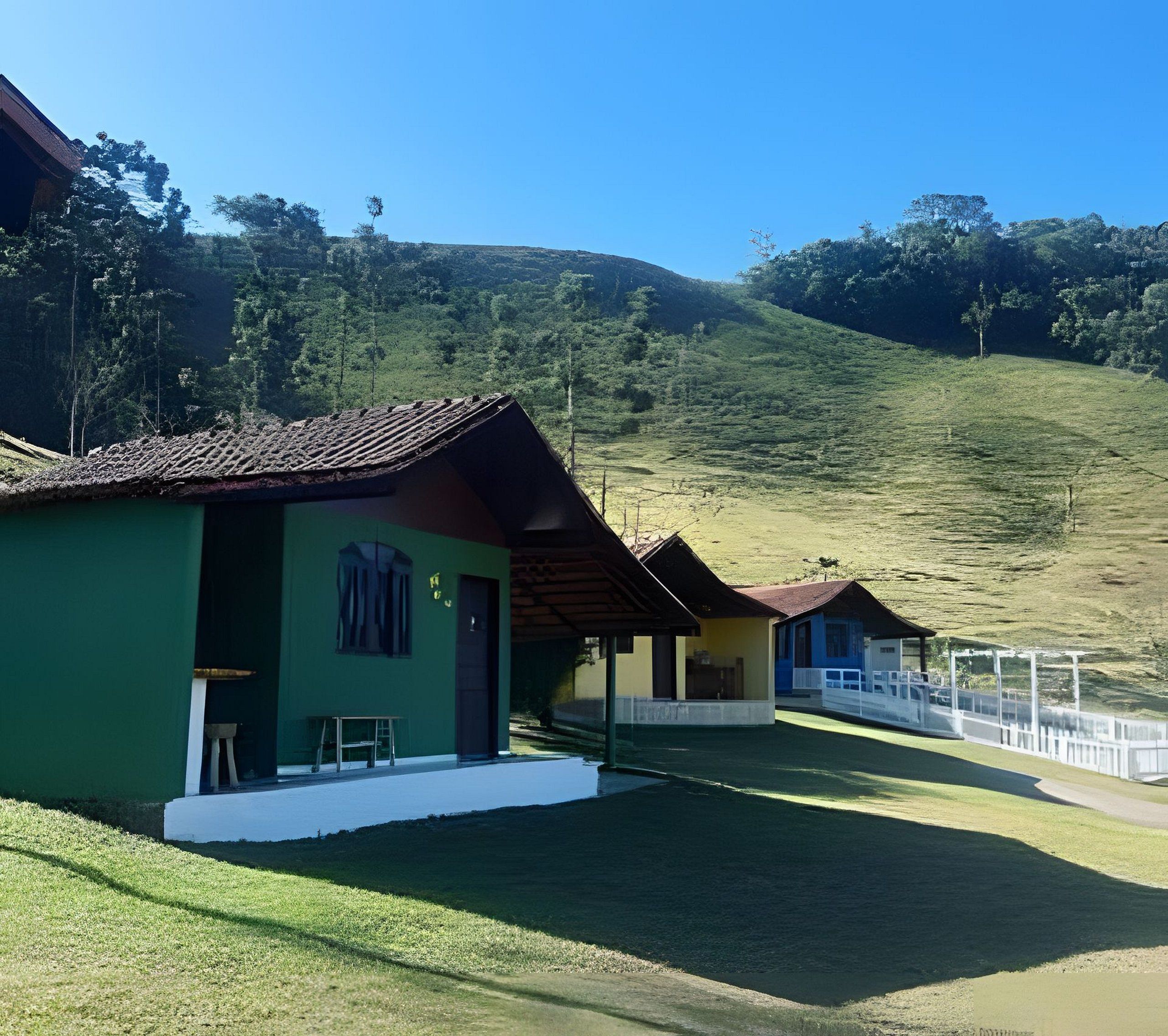 A row of small, single-story buildings with a flat roof, likely a guesthouse or lodge, situated on a grassy slope with a clear sky above.