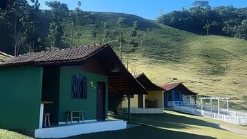 A row of small, single-story buildings with a flat roof, likely a guesthouse or lodge, situated on a grassy slope with a clear sky above.