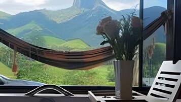 Eine Hängematte, ein Blumentopf und der Blick auf Berge durch ein Fenster.