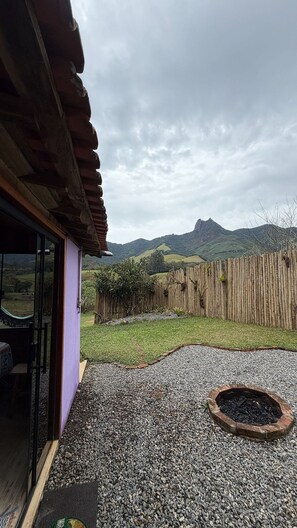 Un patio con suelo de grava, cerca de madera y vista a colinas verdes al fondo.