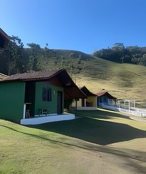 A row of green and yellow buildings with a grassy area in front, set against a hillside.