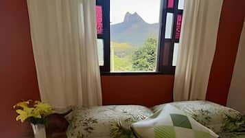 Un dormitorio con cama, cortinas, una mesita de noche y una ventana con vistas a la montaña.