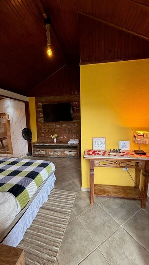 A room with a bed, a wooden table, a wall-mounted TV, and a yellow wall.