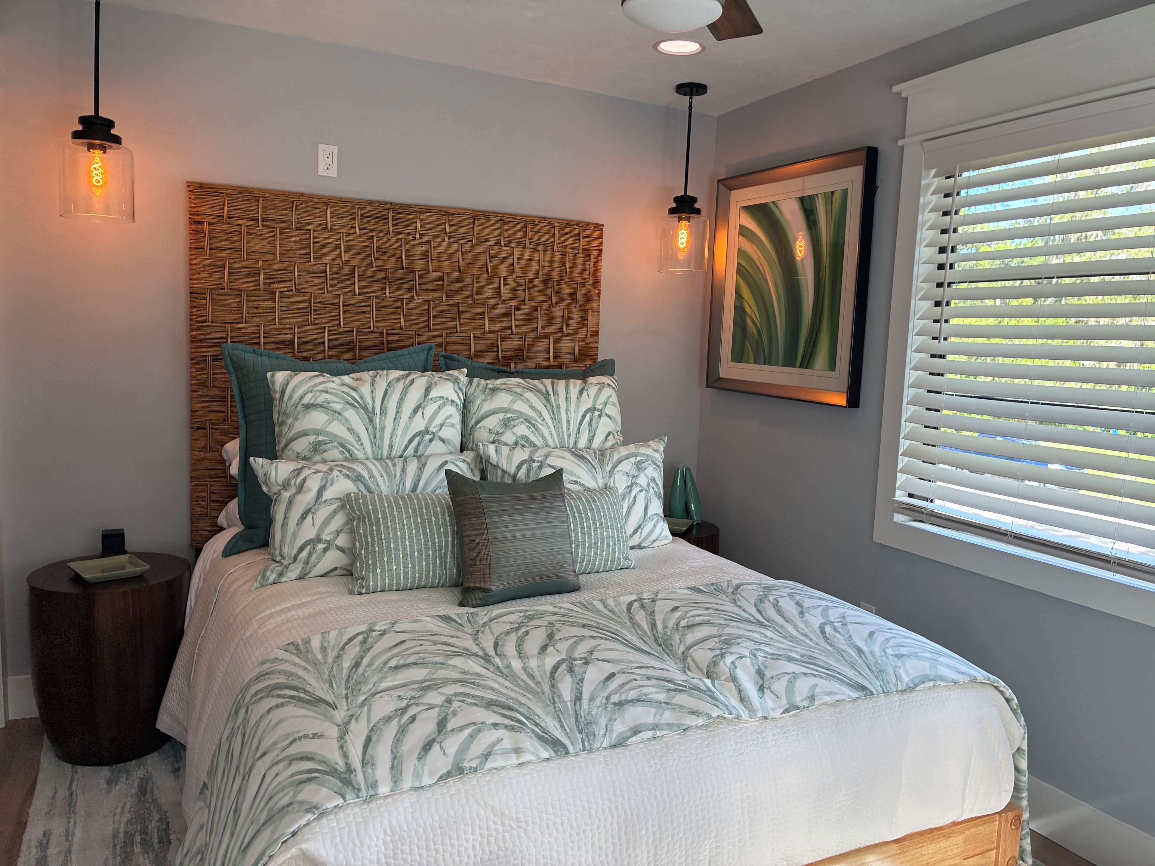 A bedroom with a bed, a headboard, bedside tables, a nightstand, a framed picture, and a window with blinds.