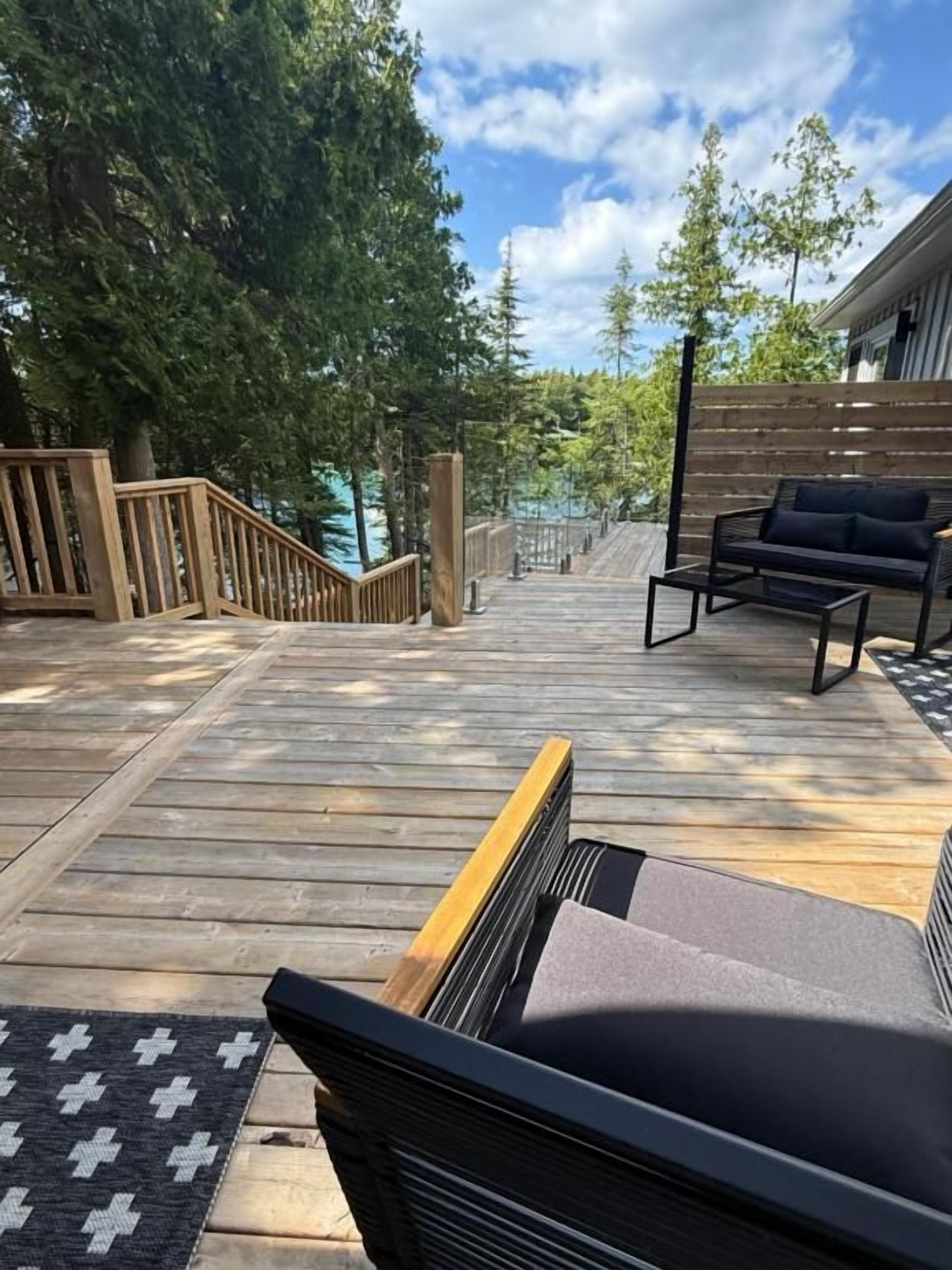 A wooden deck with a sofa and a chair, surrounded by trees and a wooden fence.