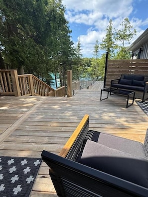 A wooden deck with a sofa and a chair, surrounded by trees and a wooden fence.