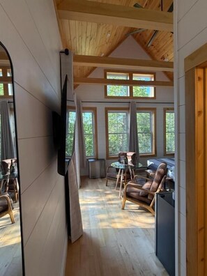 A wooden interior with a dining area, a television, and large windows.