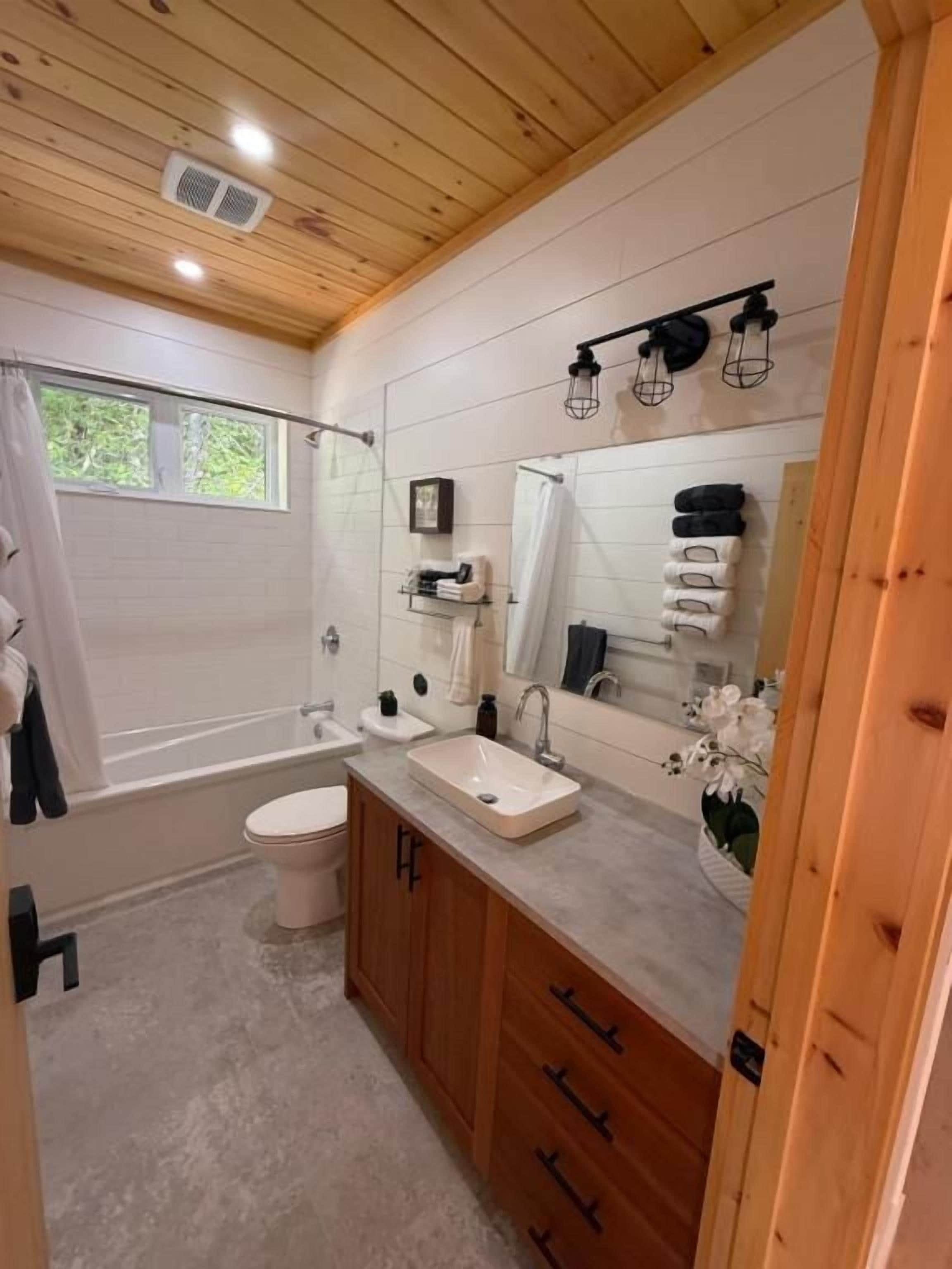 A bathroom with a bathtub, toilet, sink, and wooden cabinets.