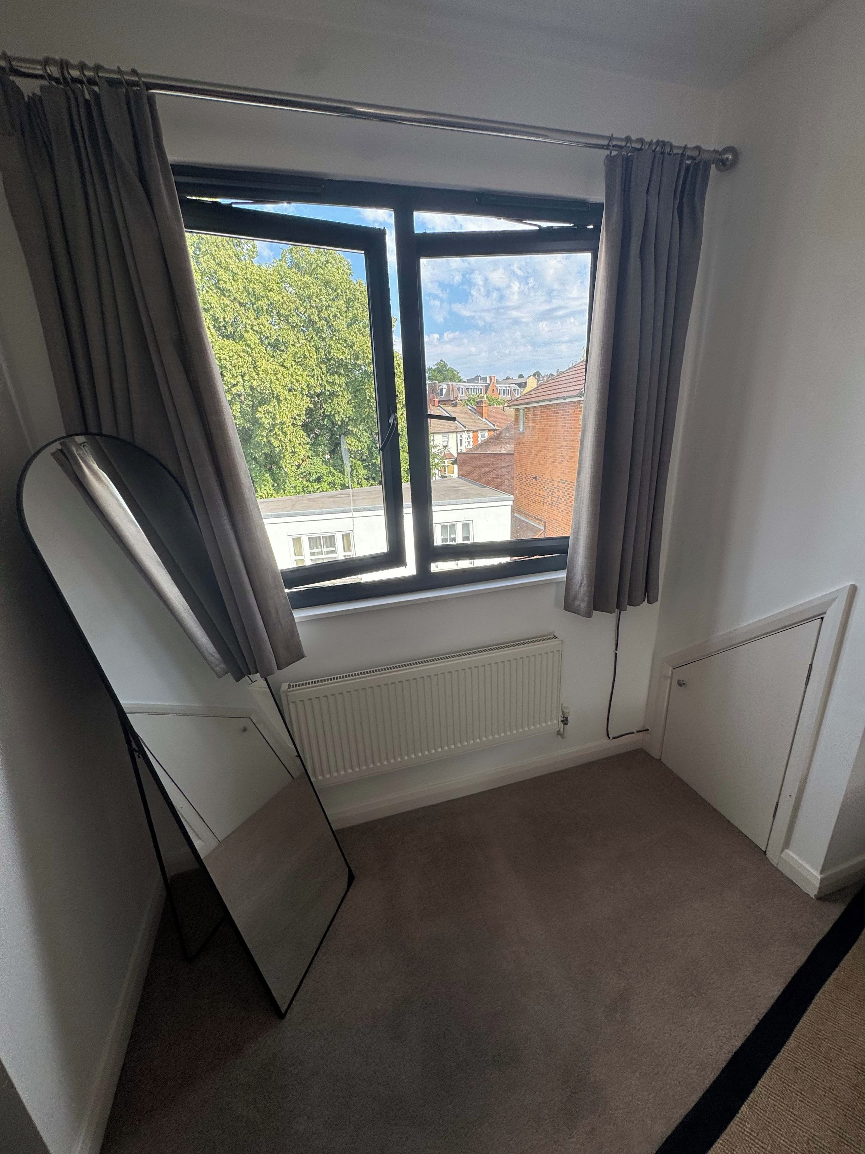 A room with a large window, a radiator, and a mirror leaning against the wall.
