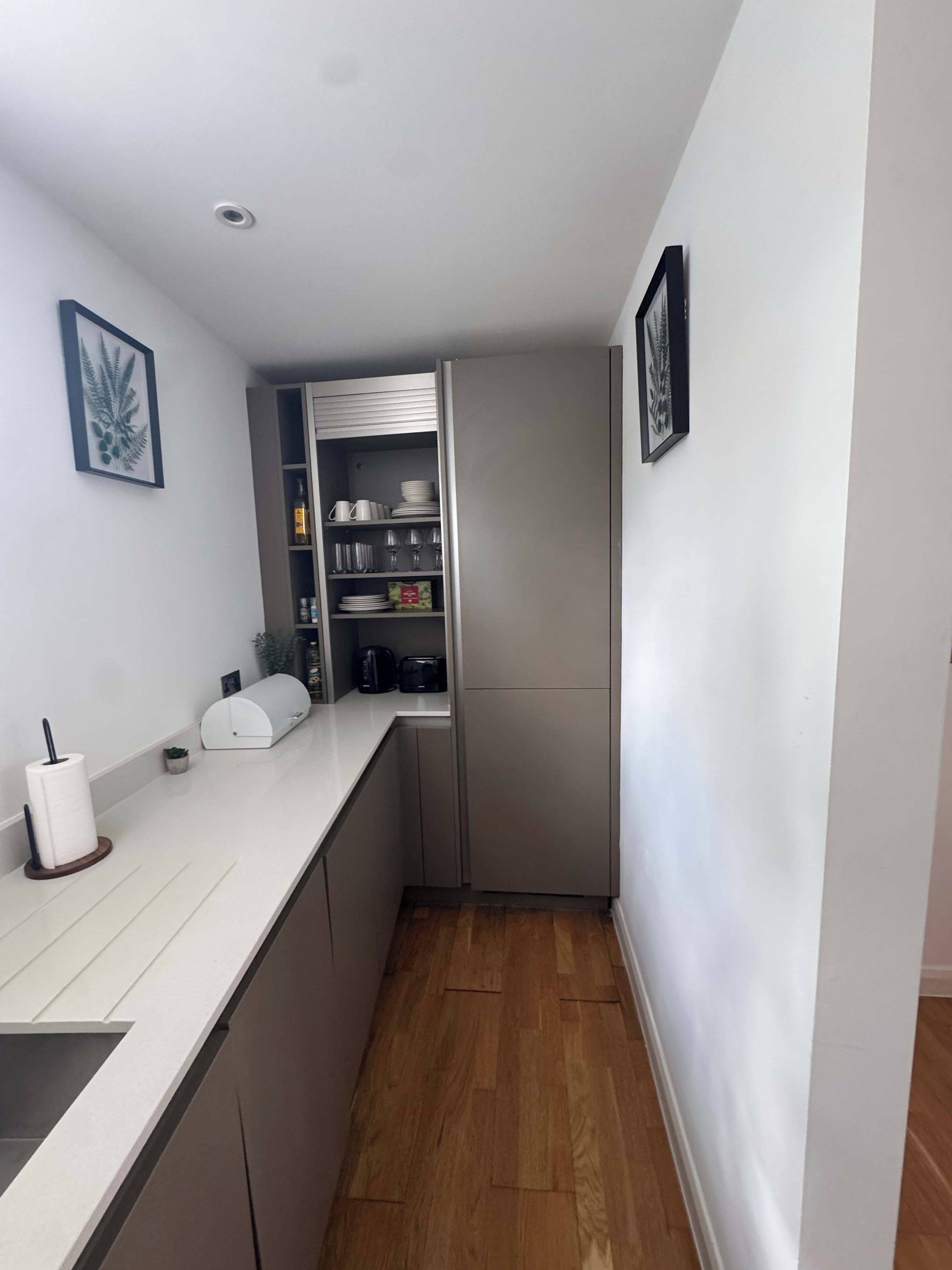 Una cocina pequeña con encimera blanca, horno integrado y suelo de madera.