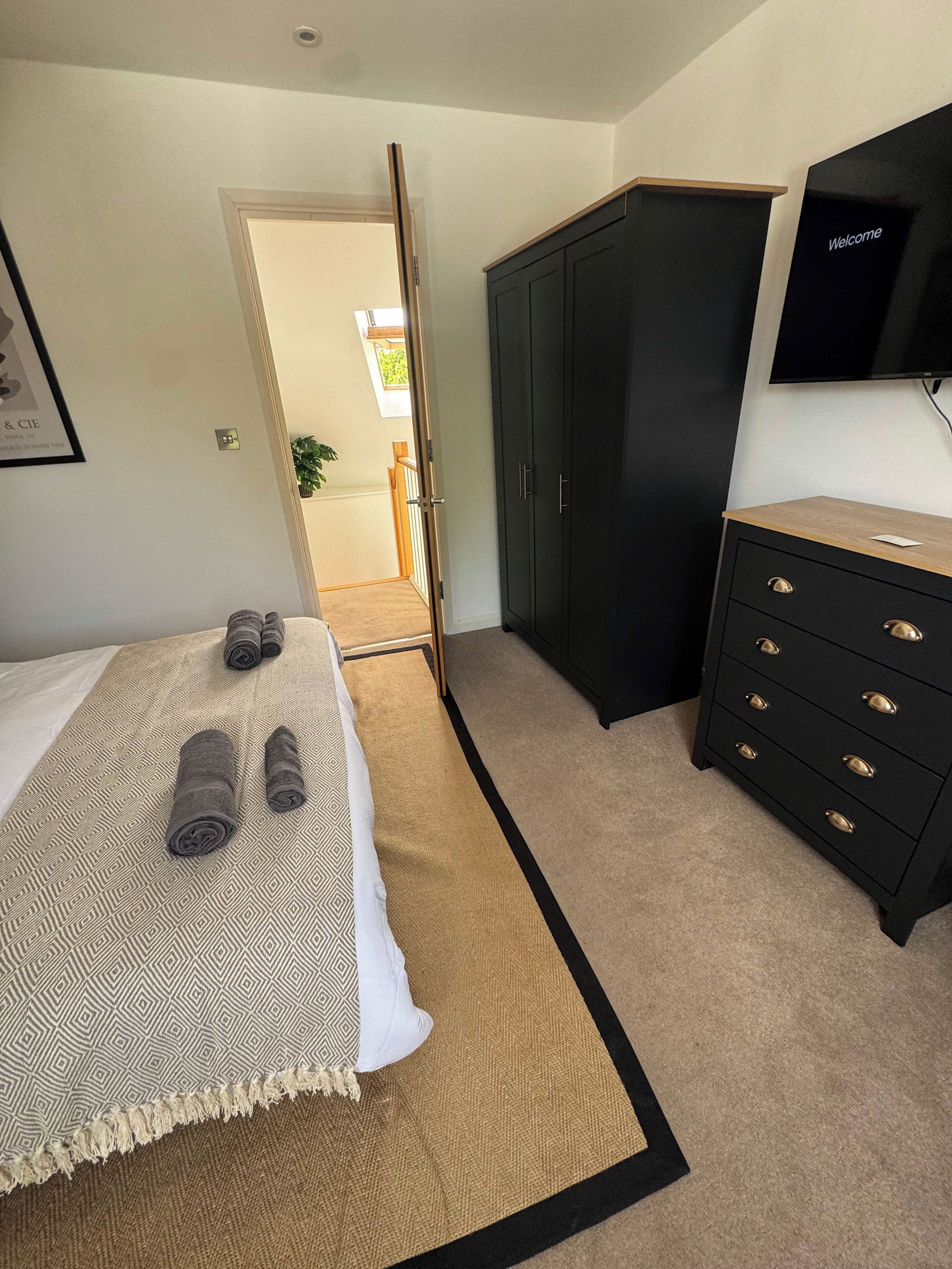 A bedroom with a bed, a wardrobe, a television, and a door leading to another room.