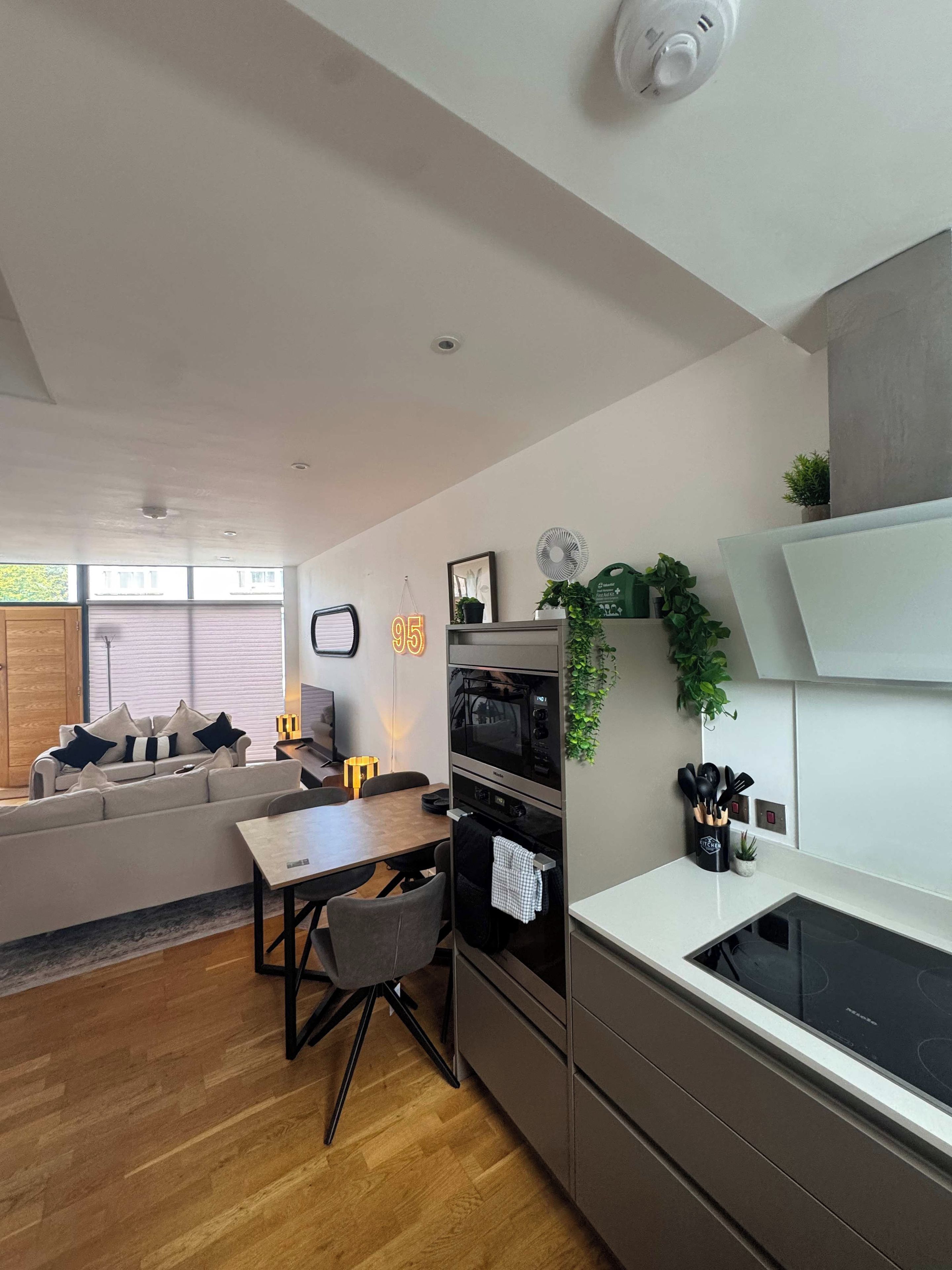 Una cucina moderna con elettrodomestici integrati, una zona pranzo con tavolo in legno e un soggiorno con divano.
