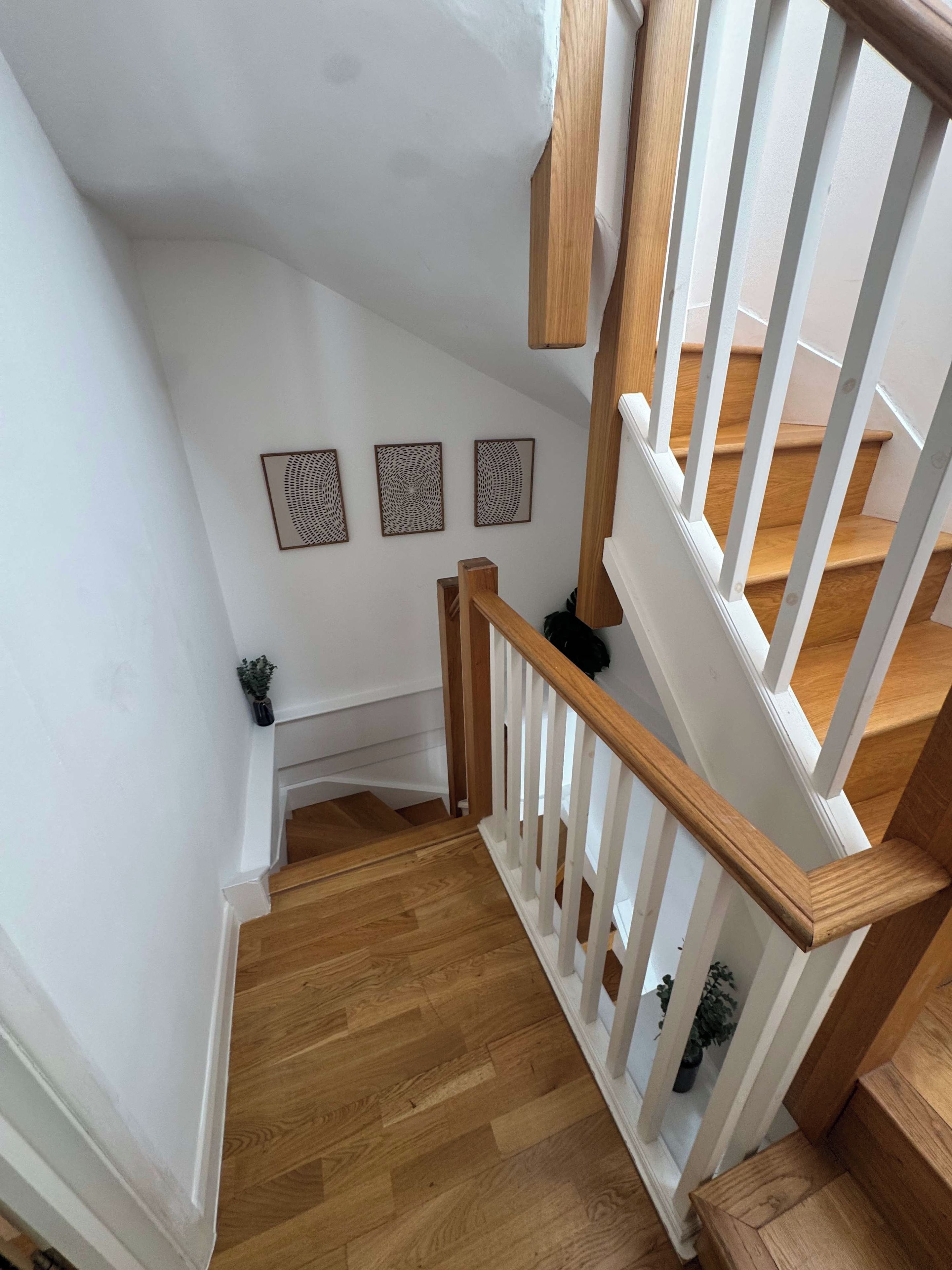 A wooden staircase with white railings and a white wall with three framed artworks.