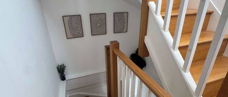 A wooden staircase with white railings and a white wall with three framed artworks.