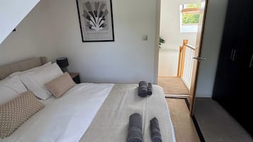 Una camera da letto con un letto, cuscini, una coperta e asciugamani arrotolati. C'è un quadro appeso al muro e una porta che dà su un balcone.