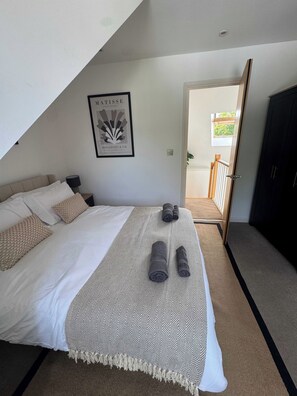Quarto com cama, travesseiros, cobertor e toalhas dobradas. Há um quadro na parede e uma porta que dá para uma varanda.