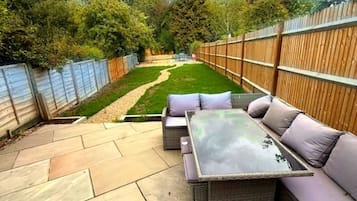An outdoor patio with a sofa and table, surrounded by a wooden fence and a garden.