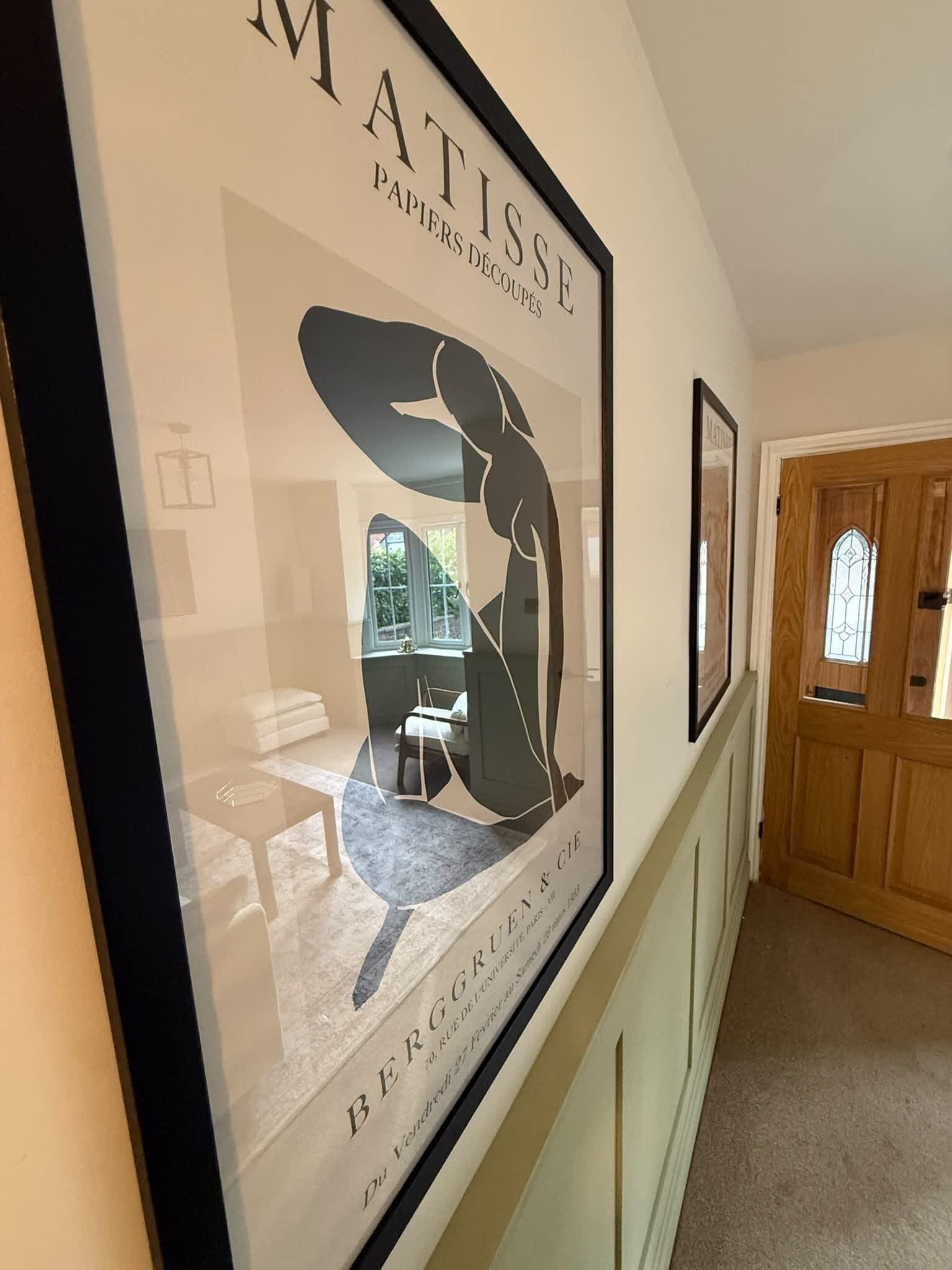 A hallway with framed artwork on the wall, a door with a window, and a carpeted floor.
