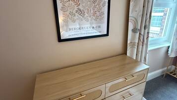 A framed artwork of a plant on a wall, a wooden dresser with drawers, and a window with curtains.