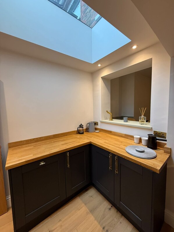 A modern kitchen with dark cabinets, a wooden countertop, and a skylight above.