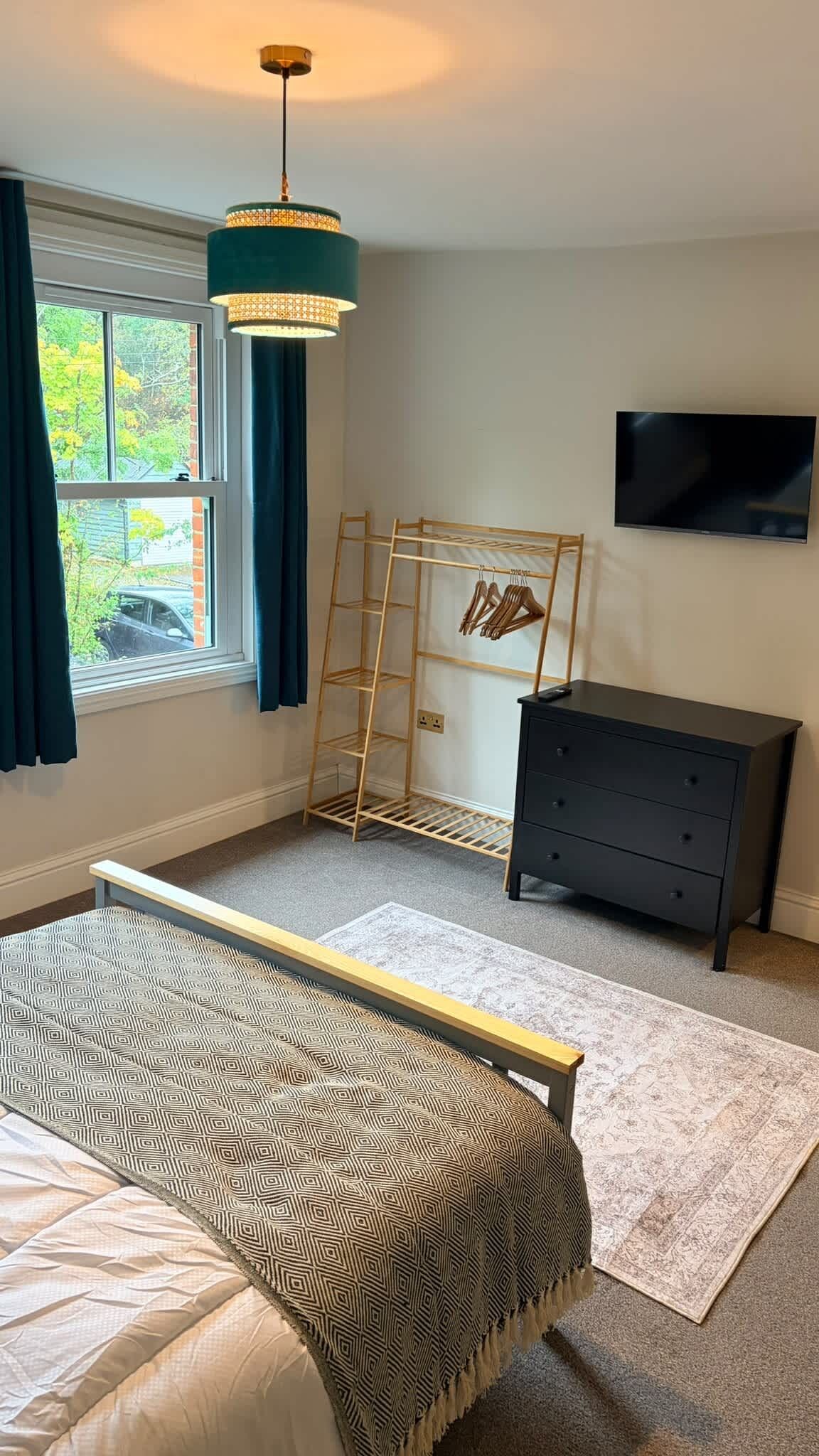 A bedroom with a bed, a dresser, a TV, and a window with curtains.