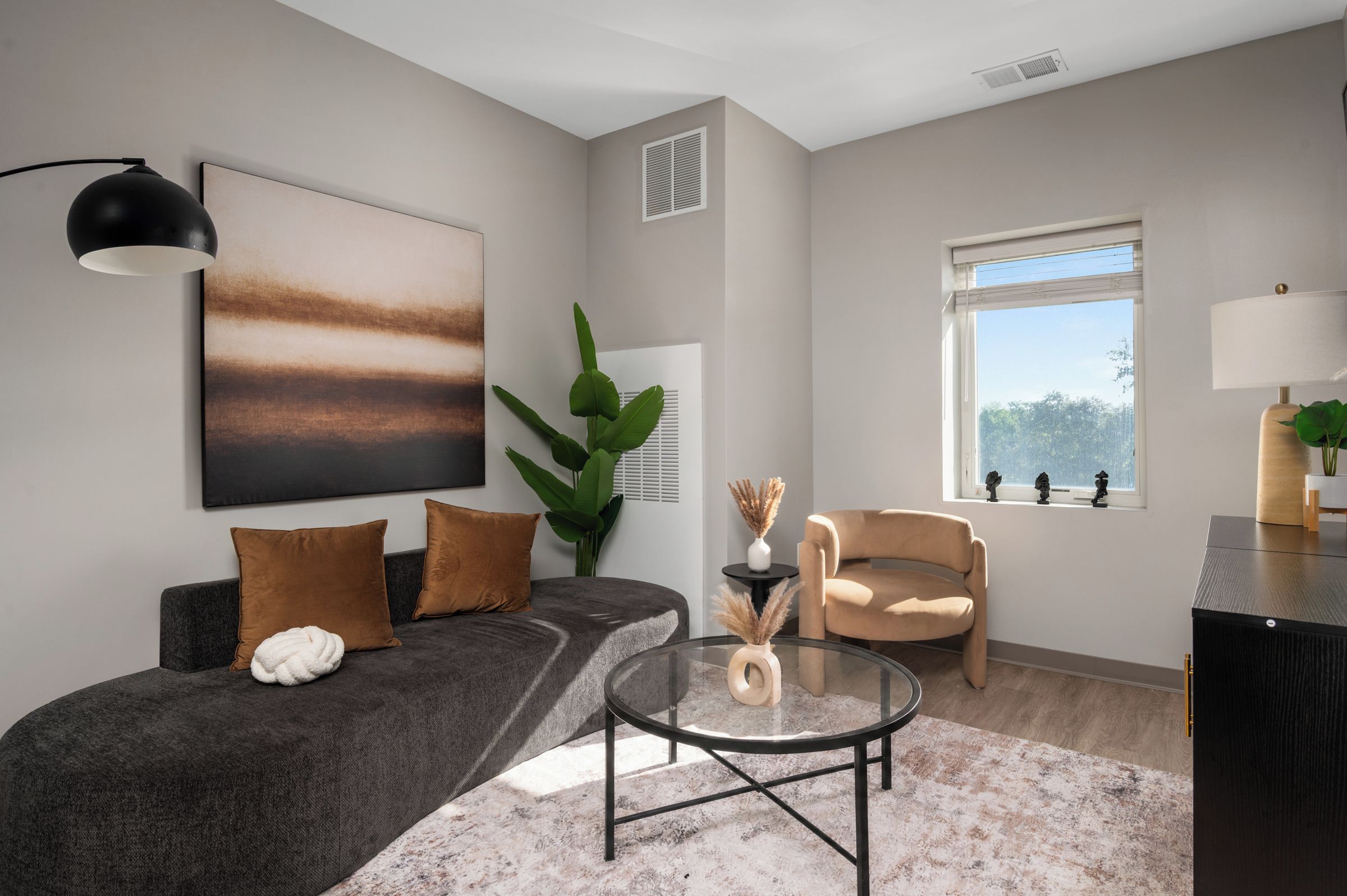 Ein modernes Wohnzimmer mit einem grauen Sofa, einem runden Couchtisch und einem beigen Sessel.