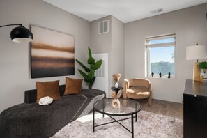 Ein modernes Wohnzimmer mit einem grauen Sofa, einem runden Couchtisch und einem beigen Sessel.