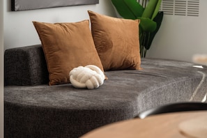 Ein graues Sofa mit zwei braunen Kissen und einem weißen, strukturierten Kopfkissen.