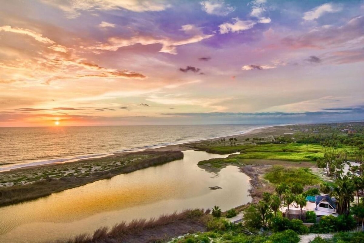Paisagem costeira com um pôr do sol, um corpo de água e um pequeno edifício com telhado.