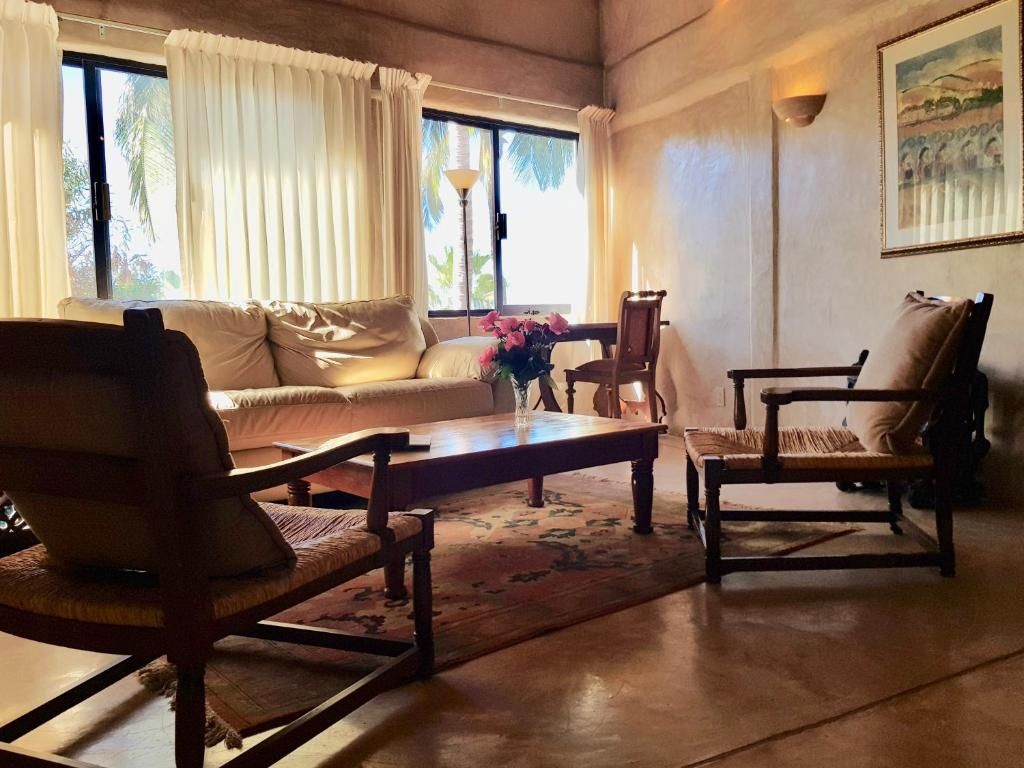 A room with a sofa, two chairs, a wooden table, and a window with curtains.