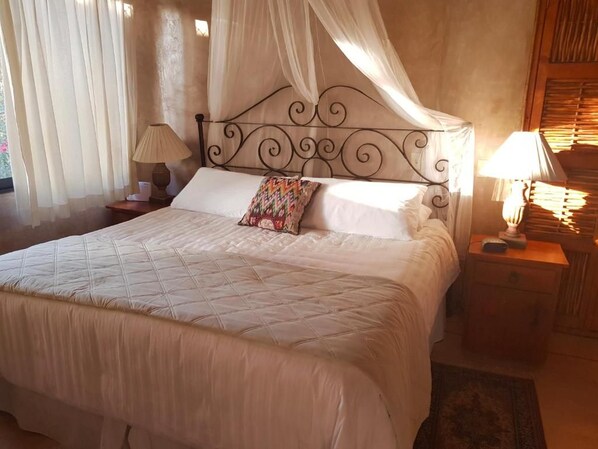A bed with a canopy, two bedside tables with lamps, and a window with curtains. - Alegria Suites La Poza Beach (Todos Santos)