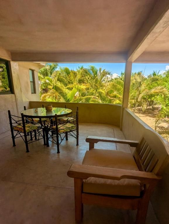 A covered outdoor seating area with a table and chairs, overlooking a tropical landscape with palm trees.