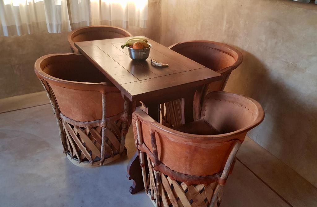 A wooden table with four terracotta chairs, a bowl of fruit, and a small container on the table.