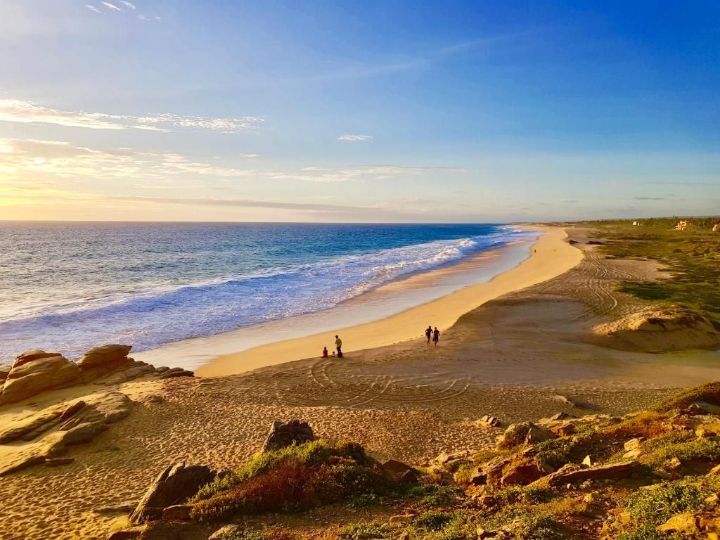 A beach with a clear sky, a sandy shore, and a few people walking.