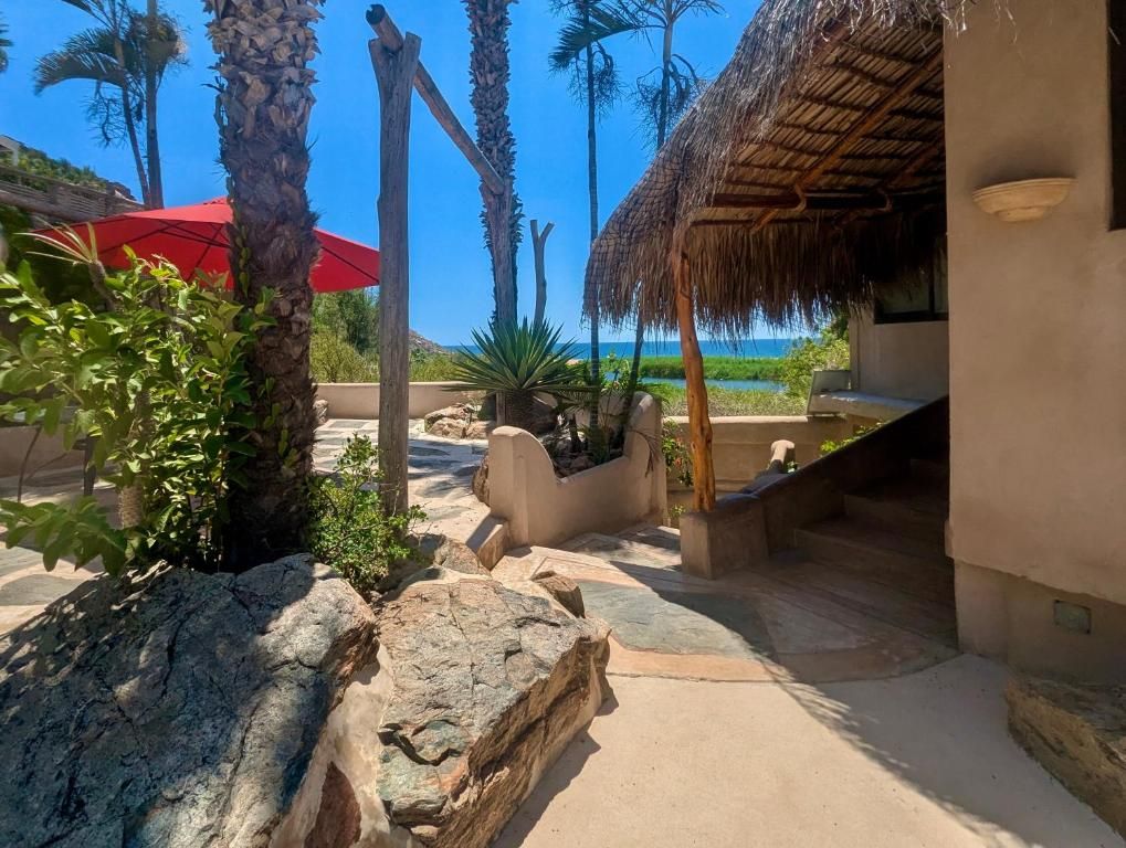 An outdoor patio area with a thatched roof, palm trees, and a view of the ocean.