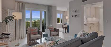 A modern living room with a sofa, armchairs, and a coffee table. There is a view of the outdoors through large windows.